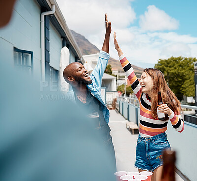 Buy stock photo A cheerful african american man doing a high five gesture with a mixed race woman while smiling and laughing outside on a sunny day while enjoying a drink of beer in a glass bottle. Black male and his hispanic friend having fun and celebrating at a party