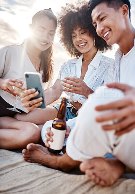 A group three multiracial friends relaxing and using a phone at the beach while having alcoholic drinks