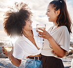 Two young mixed race female friends hanging out and having wine at the beach. Hispanic women having a glass on wine outdoors