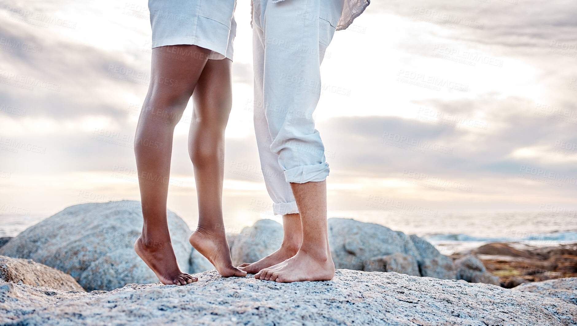 Buy stock photo Rock, legs and couple on beach for love, embrace and bonding together on vacation in California. People, feet and dating in relationship with commitment, caring and adventure holiday in ocean outdoor