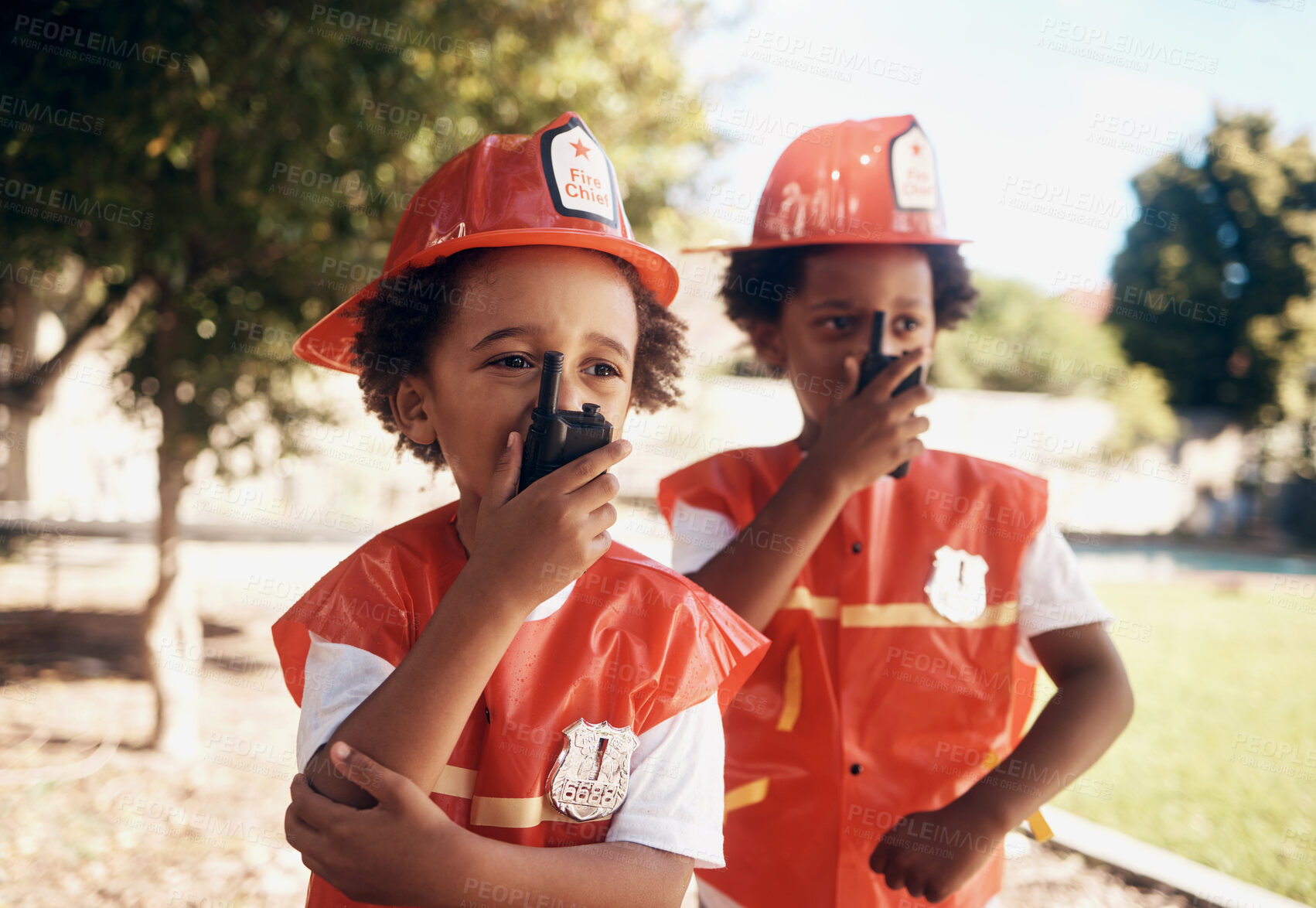 Buy stock photo Two cute little african american boys having fun while playing outside in the backyard dressed as firemen and using wireless devices to talk to one another, playing pretend with a radio