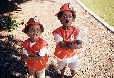 Two cute little african american boys having fun while playing outside in the backyard pretending to be firemen. Two young black male brothers having fun outdoors looking shocked and surprised while playing