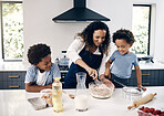 Adorable little boy with afro baking in the kitchen at home with his mom and brother. Cheerful mixed race woman mixing ingredients with the help of her little boys. Baking is a bonding activity