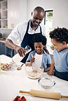 Adorable African American little boy with afro baking in the kitchen at home with his dad and brother. Cheerful Black man holding milk and mixing ingredients while bonding with his little boys