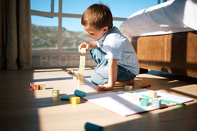 Buy stock photo Little boy building a tower with wooden blocks. Adorable caucasian child stacking toys while developing fine motor skills and hand-eye coordination. Boy playing with building blocks or wooden cubes