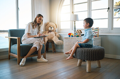 Buy stock photo An adorable little boy sitting on a chair while talking to a caucasian therapist. Cute little boy talking to a psychologist. Child checking in with a counsellor at a foster home before being adopted 