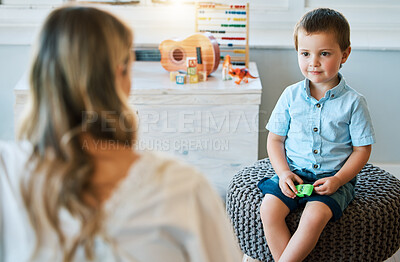 An adorable little boy sitting in his bedroom at home and talking to his mother. Happy male child bonding with his mom. Rearview of a blonde woman spending quality time with her young son on a weekend