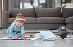 Adorable little girl sitting on the floor and writing or drawing with pencil at home. Small caucasian girl doing homework or  being creative