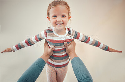 Adorable little girl pretending to fly with arms outstretched while being lifted in the air by parent. Cute kid having fun and bonding with father at home