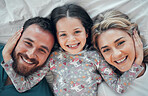 Happy carefree caucasian family in pyjamas from above lying cosy together in bed at home. Loving parents with their little daughter. Adorable young girl hugging her mom and dad's face during bedtime