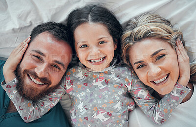 Happy carefree caucasian family in pyjamas from above lying cosy together in bed at home. Loving parents with their little daughter. Adorable young girl hugging her mom and dad\'s face during bedtime