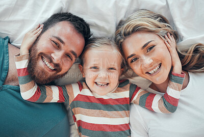 Happy smiling caucasian family of three looking cosy together in bed at home. Loving parents with their little daughter. Adorable young girl hugging her mom and dad\'s face and taking a selfie
