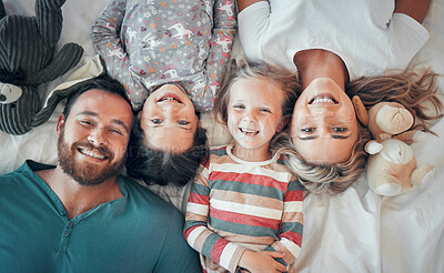 Above shot of happy caucasian family lying together on bed. Happy faces of family with two daughter spending quality time together at home. Couple having fun with their two daughters