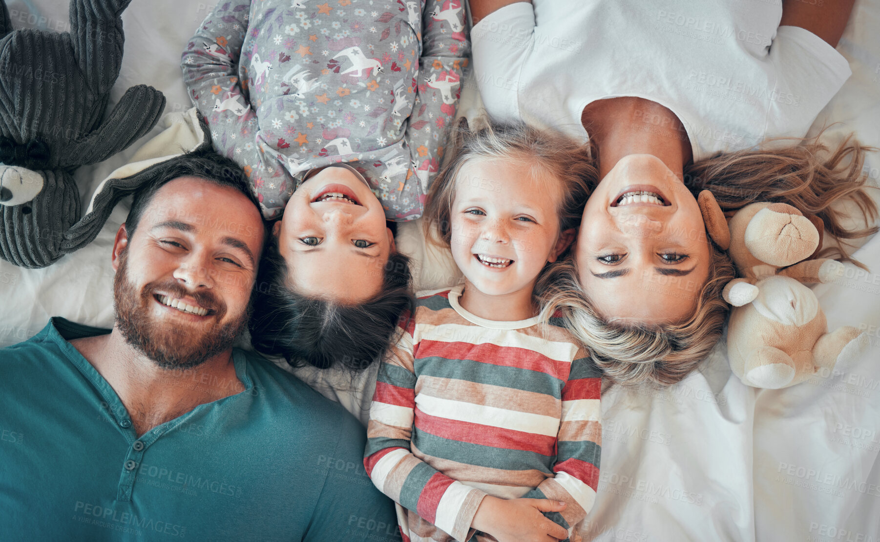 Buy stock photo Above shot of happy caucasian family lying together on bed. Happy faces of family with two daughter spending quality time together at home. Couple having fun with their two daughters