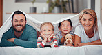 Happy caucasian family of four in pyjamas lying cosy together in a row on a bed with blanket over their heads at home. Loving parents with two kids. Adorable girls bonding with mom and dad at bedtime