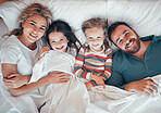 Happy caucasian family of four in pyjamas from above lying cosy together in bed at home. Loving parents with their two little kids. Adorable young girls bonding with their mom and dad during bedtime