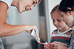 Caucasian mom squeezing toothpaste from a tube onto toothbrushes of two little girls in pyjamas at home. Teaching kids good hygiene habits. Brush twice daily to prevent tooth decay and gum disease