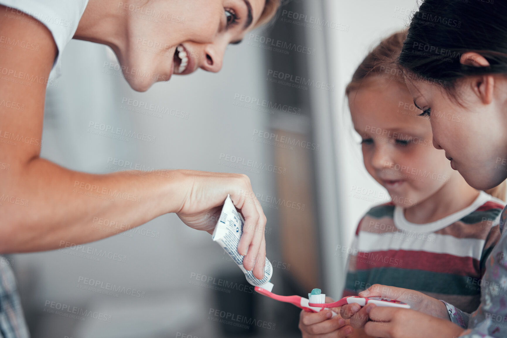 Buy stock photo Caucasian mom squeezing toothpaste from a tube onto toothbrushes of two little girls in pyjamas at home. Teaching kids good hygiene habits. Brush twice daily to prevent tooth decay and gum disease