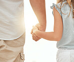 Rear view of a caucasian father holding the hand of his little girl while standing outdoors on a sunny day with a flare in between them. Father and young daughter showing affection and love by holding hands, a symbol of a loving family who are