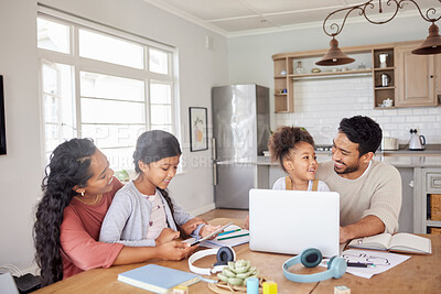 Mixed race family sitting together doing homework and using digital devices at kitchen table. Couple sitting at home with two daughters and using modern technology for online learning