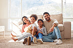 Portrait of two happy parents bonding with their daughters in the lounge, sitting on the floor. Smiling young family relaxing at home, enjoying time together. Mother and father holding their daughters
