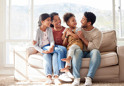 Buy stock photo Fullbody shot of a happy, young affectionate family of four sitting on the sofa in their living room at home. Two little sisters bonding with their mother and father. Having daughters is the best