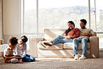 Happy family relaxing at home. Smiling young parents with girls on a sofa, watching their cute little children play and have fun with a digital tablet on the floor in the living room with a window