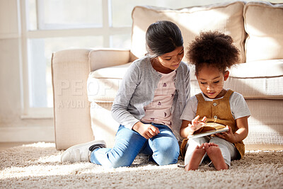 Buy stock photo Two little mixed race sisters sitting on the floor and playing on digital tablet together at home. Hispanic female friends learning to use a digital tablet together