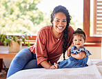 Portrait of young mixed race mother sitting with her adorable baby girl on the bed in a bedroom at home. Hispanic woman spending time with her cute little daughter on a bed at home