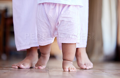 Little baby girl walking with the help of her parent. Closeup of the feet of a small child walking at home with her mother behind her. Mother helping her daughter walk, take her first steps at home.