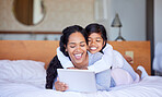 Young happy mixed race mother and her daughter using a digital tablet together in a bedroom. Hispanic mom teaching her little daughter how to use a digital tablet at home