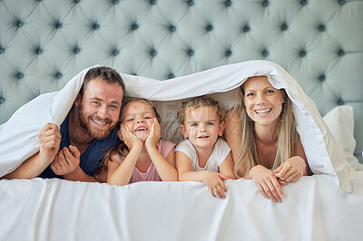 Buy stock photo A happy family in bed under a blanket at home. Portrait of  smiling young parents having fun with children in the bedroom, covering with a duvet. Cute little girls playing with their mother and father
