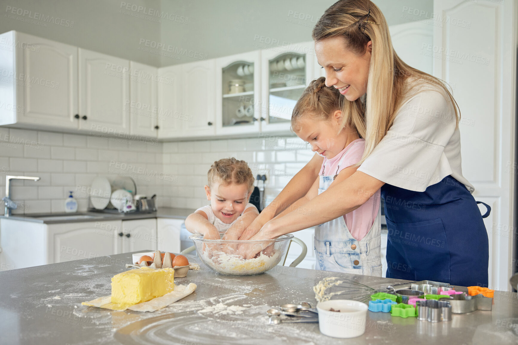 Buy stock photo Caucasian caring mother and little daughters baking together in a kitchen at home. Mom teaching girls how to make dough in a messy kitchen. Sisters learning how to bake with their mom
