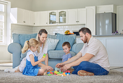 Buy stock photo Happy caucasian family of four smiling while playing with toys and sitting on the floor together in the lounge at home. Two loving parents spending time with their little carefree son and daughter