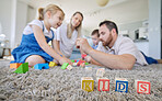 Caucasian family of four playing with toys and sitting on the floor together in the lounge at home. Parents spending time with their little children. Blocks on a carpet spelling out a word