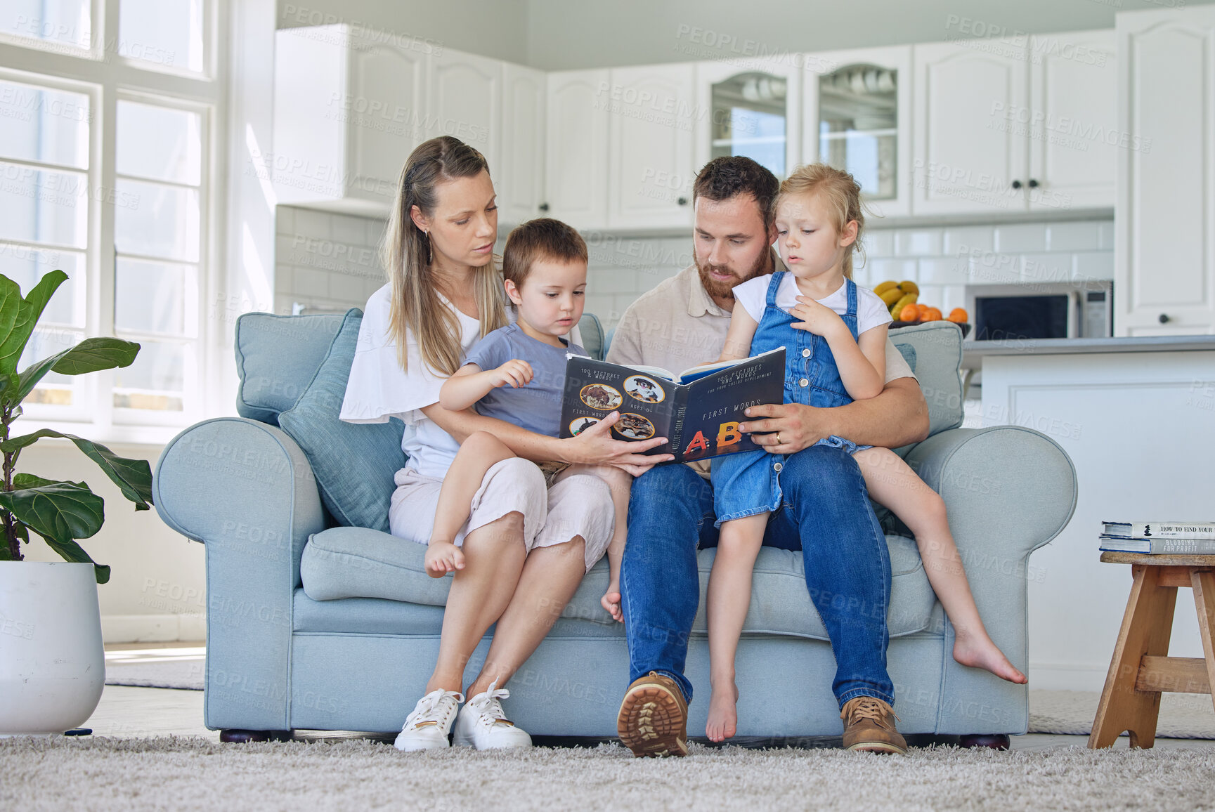 Buy stock photo Caucasian family reading a book together on the couch at home. Mother and father teaching their little son and daughter how to read. Brother and sister learning their alphabet with their parents