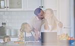 husband kissing wife on the cheek. Family relaxing in the kitchen. Woman working from home on laptop. Mother teleworking with children.  Happy family at home together. 