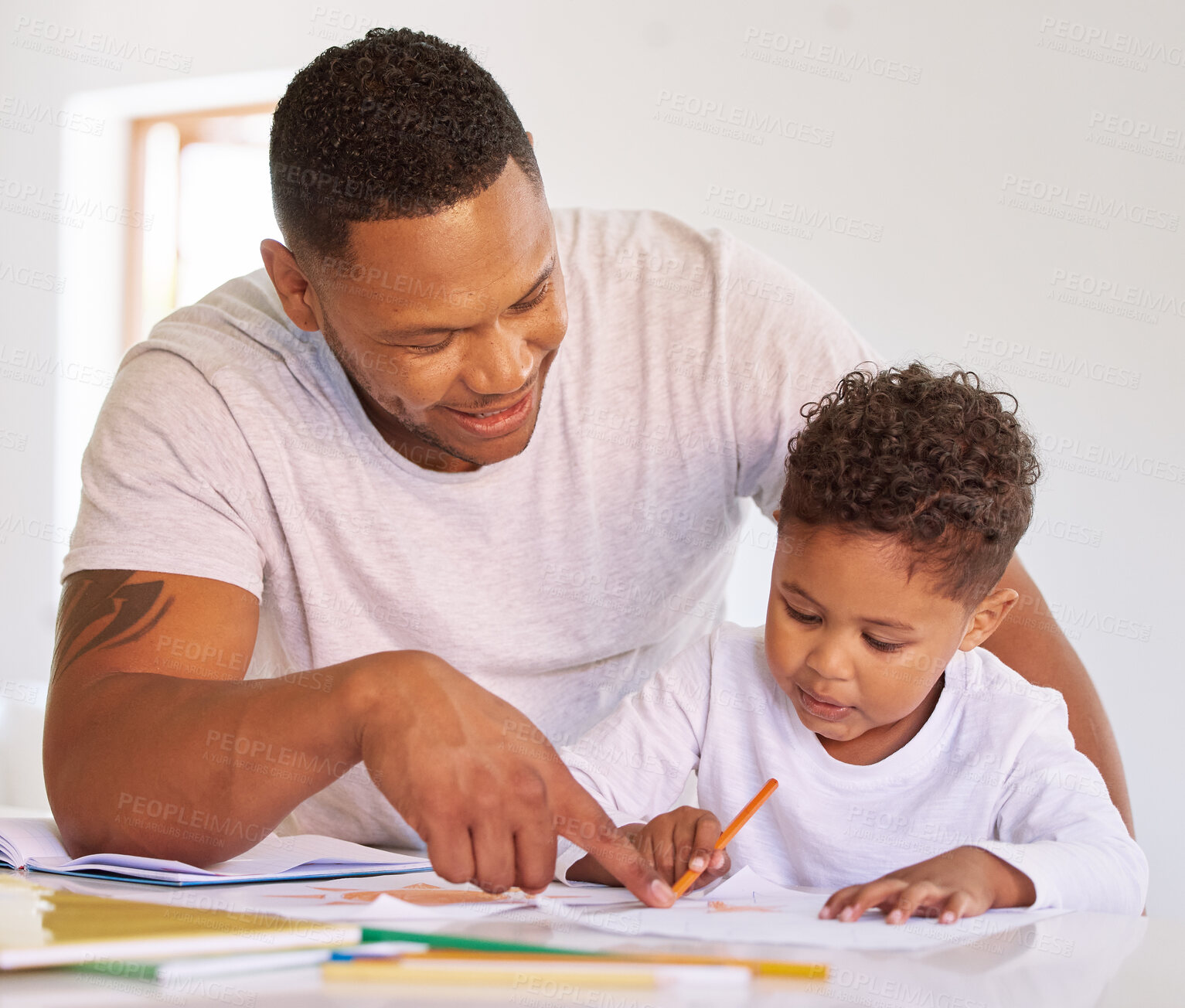 Buy stock photo Mixed race boy learning and studying in homeschool with dad. Man helping his son with homework and assignments at home. Parent teaching child to colour and write at home during lockdown