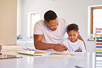 Mixed race boy learning and studying in homeschool with dad. Man helping his son with homework and assignments at home. Parent teaching child to colour and write at home during lockdown