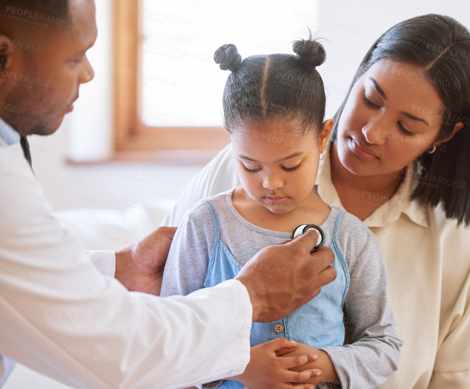Buy stock photo Sad little girl at doctor's office. Sick girl sitting with mother while male paediatrician listen to chest heartbeat. Male doctor examining child with stethoscope. Mom holding kid during doctor visit