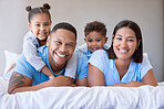 Portrait of a smiling boy and girl lying on their parents in a bed at home. Mixed race couple bonding with their son and daughter. Hispanic siblings enjoying free time with their mother and father