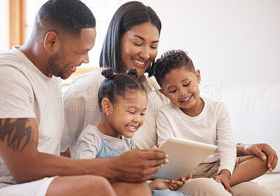 Happy mixed race smiling family of four bonding on a sofa while streaming movies on the internet using a digital tablet at home. Young couple looking cheerful with their daughter and son