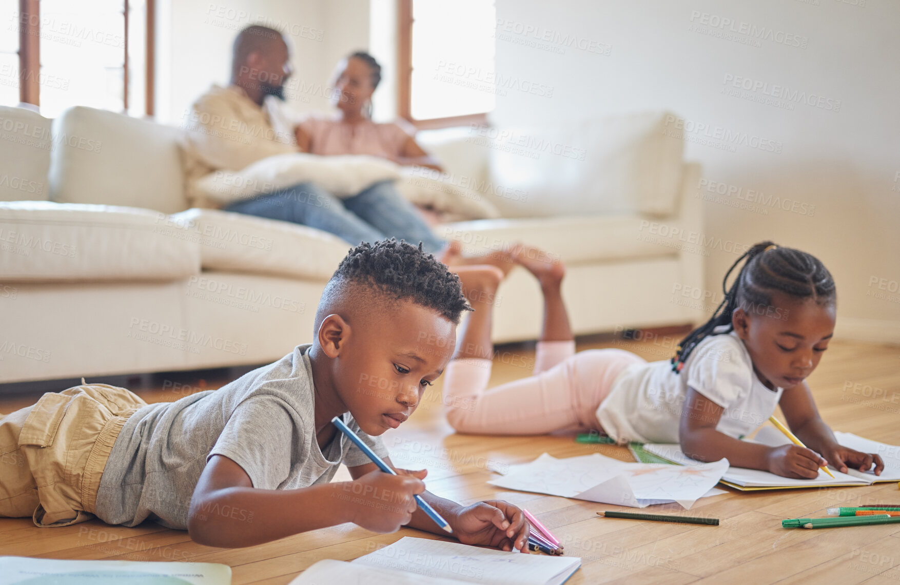 Buy stock photo Little boy and girl drawing with colouring pencils lying on living room floor with their parents relaxing on couch. Little children sister and brother siblings colouring in during family time at home 