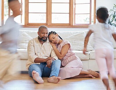 Tired African American couple sitting on the lounge floor looking tired and drained while their hyper children plays around them. Two black siblings having fun while their exhausted parents relax