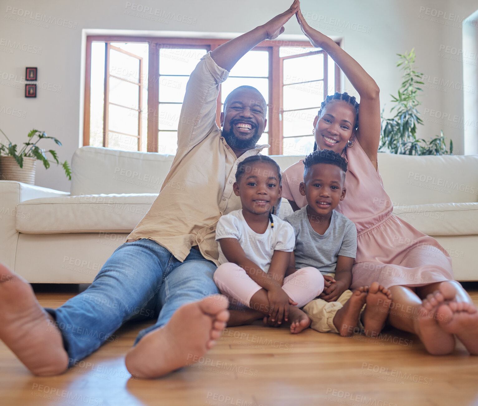 Buy stock photo A young african american couple sitting with their children at home and making a house gesture over their children at home