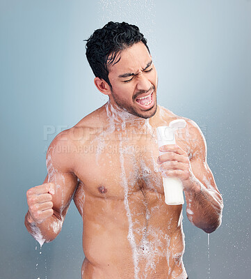 One young mixed race man singing in the shower using a bottle as a mic against a blue studio background. Cheerful hispanic guy having fun doing his morning hygiene routine in the shower