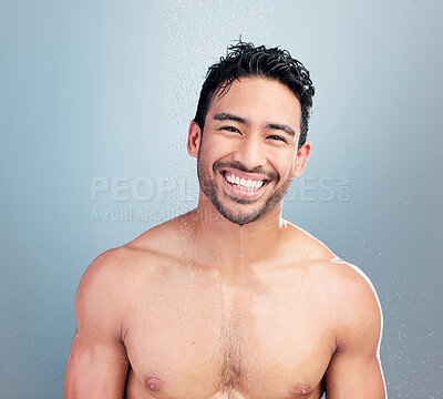 Buy stock photo Portrait of one sexy muscular young mixed race man taking a refreshing hot shower against a blue studio background. Fit smiling guy washing hair and body under clean running water for good hygiene