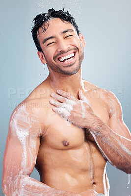 Buy stock photo Portrait of one muscular young mixed race man taking refreshing hot shower against a blue studio background. Fit smiling guy washing hair and body with soap under clean running water for good hygiene