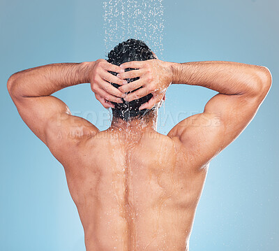 Buy stock photo Rear view of a muscular man showering alone in a studio and washing his hair against a blue background. Fit and strong mixed race man standing under pouring water. Hispanic athlete enjoying hot shower