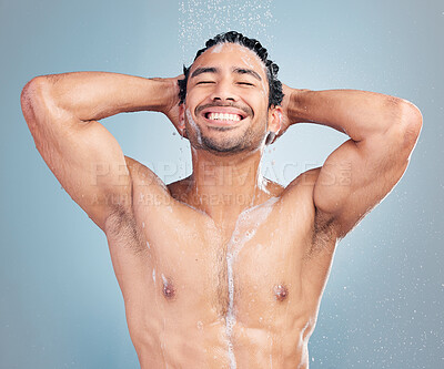Smiling muscular asian man showering alone in a studio and washing his hair against a blue background. Fit and strong mixed race man standing under pouring water. Hispanic athlete enjoying hot shower